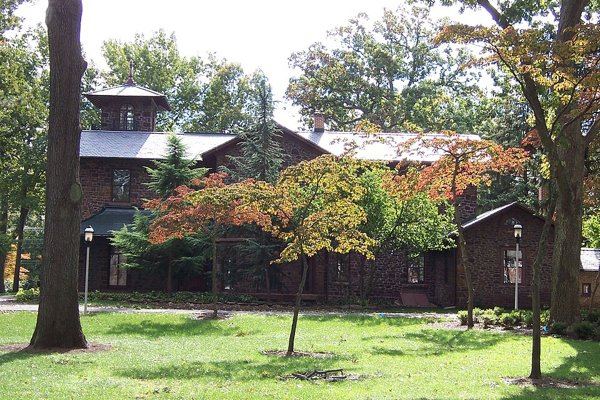 Hollybush, a dark stone house with a square tower, seen across a green lawn through trees with orange fall leaves.