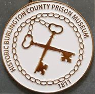 A round enamel badge reading Historic Burlington County Prison Museum, 1811, with two crossed skeleton keys inside a ring of chain links.