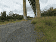 Drone footage flying low down a gravel lane between two tall concrete piers under the Reedy Point Bridge