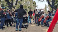 An orchestra with a conductor and cellos set up on a lawn under trees at RoxYunk Porchfest
